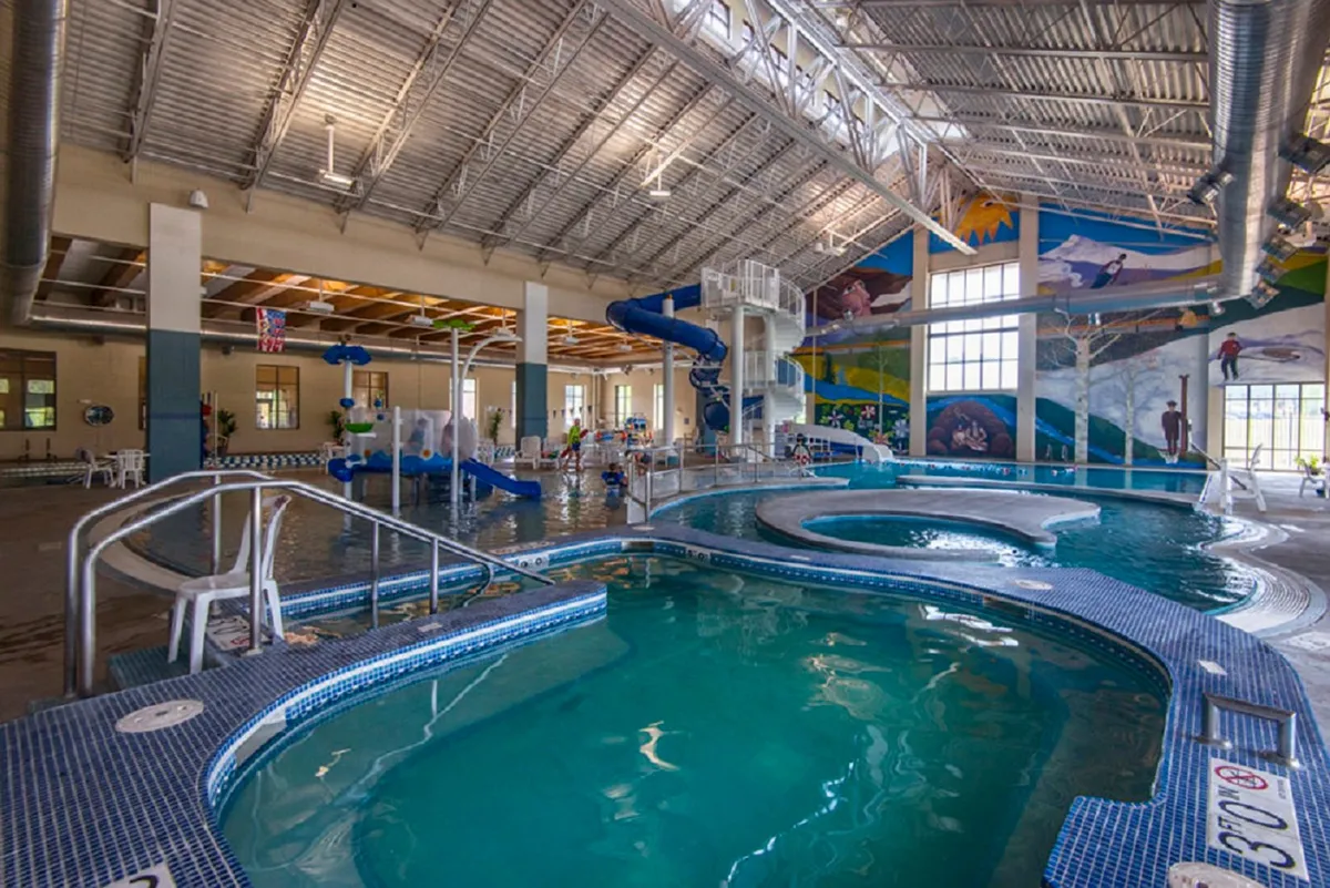 A lively indoor water park scene, featuring water slides, swimming pools, and children joyfully playing amid colorful murals. The space is buzzing with energy, reflecting memorable summer outings and family bonding moments.