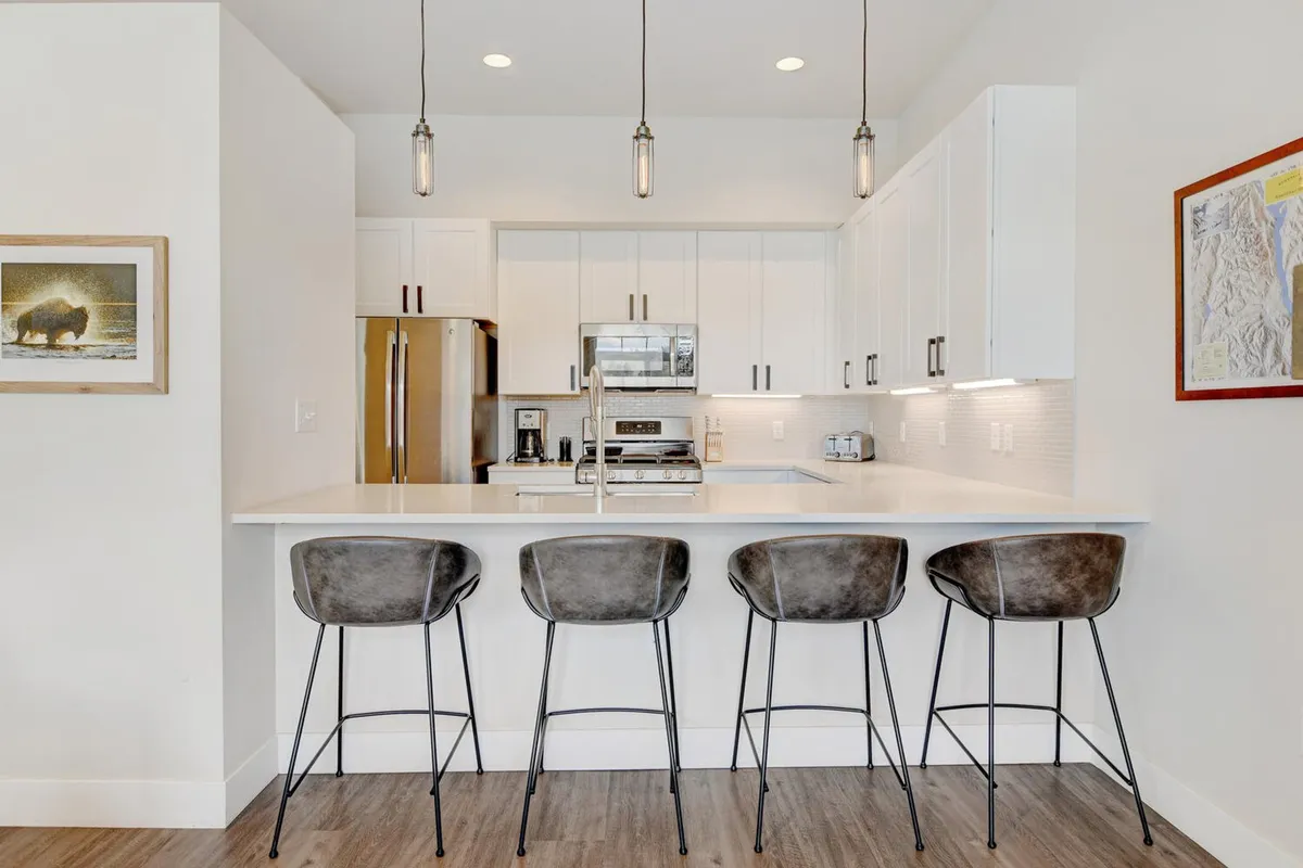 A modern kitchen with a central island, bar stools, stainless steel appliances, and elegant lighting. The space is designed for both cooking and socializing, with clear sightlines to adjoining areas.