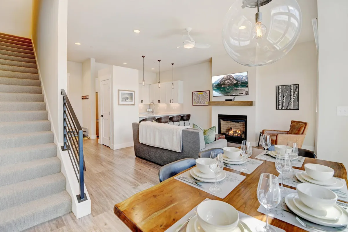 A cozy and inviting interior scene showcasing a dining table set for a meal, a comfortable seating area, and a fireplace. The fireplace is prominent, recalling the programmable gas fireplace and overall warmth provided by radiant in-floor heating.