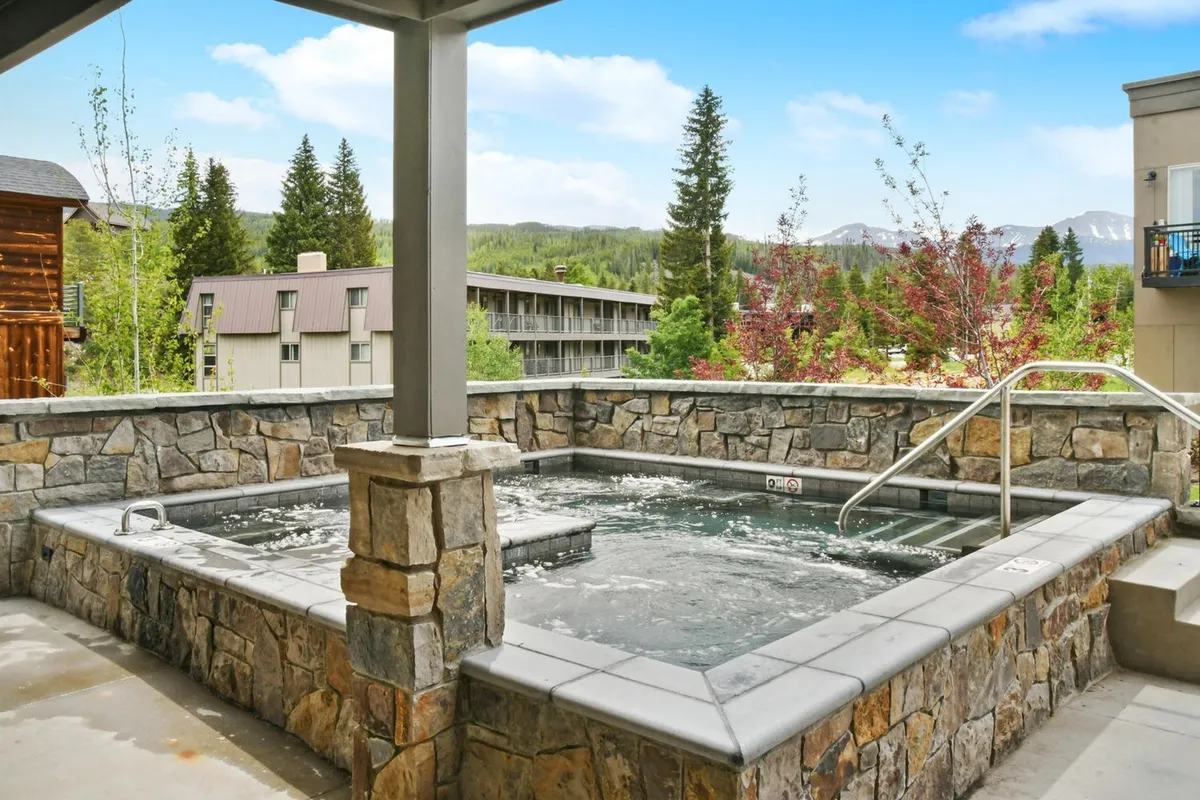This exterior image features the community hot tub nestled within a stone structure, surrounded by scenic landscape. The tranquil mood highlights the hot tub area at sunset, inviting guests to relax and socialize while enjoying beautiful views.