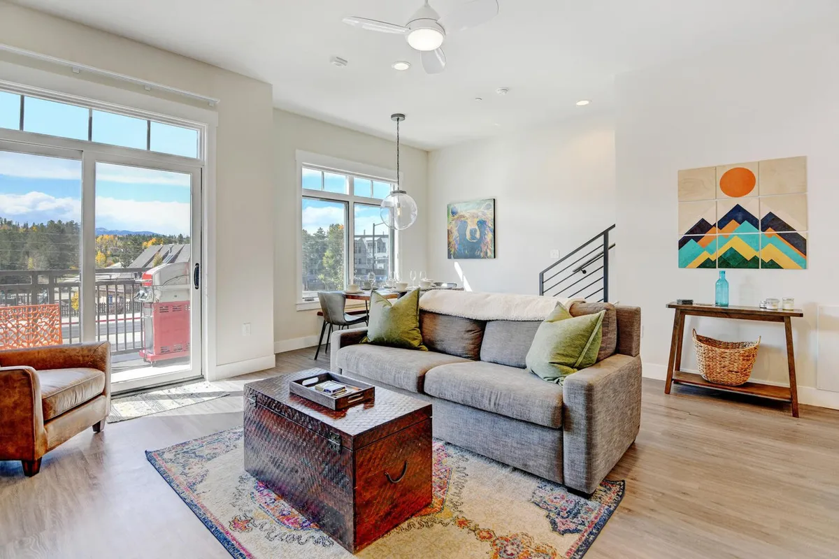 A comfortable living area with a plush sofa, coffee table, and large windows that let in plentiful natural light. Artwork on the wall and cozy furnishings create an inviting space for relaxing or socializing after exploring town.