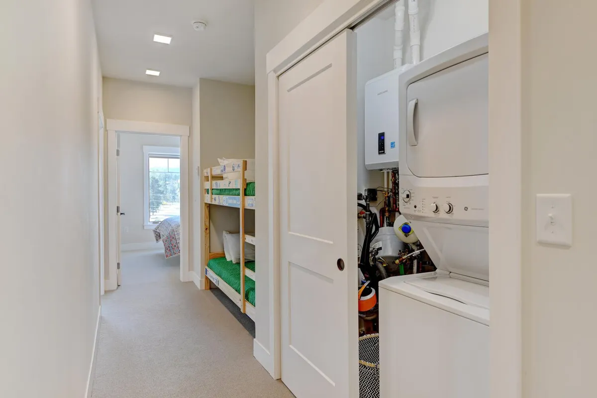 A practical family space featuring built-in bunk beds, laundry appliances (washer and dryer), and a doorway leading to another room. The mood is functional yet cozy, catering to the needs of families with children and supporting longer stays.