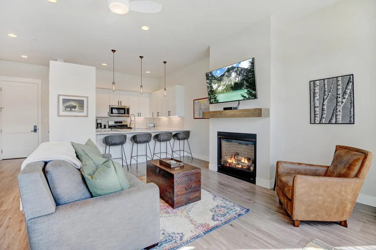 This image captures a spacious, open-plan living area featuring a comfortable sofa, a modern fireplace, a kitchen island, and a large television. The setting exudes warmth and sociability, inviting guests to relax, watch TV, or gather together after a day of adventure.