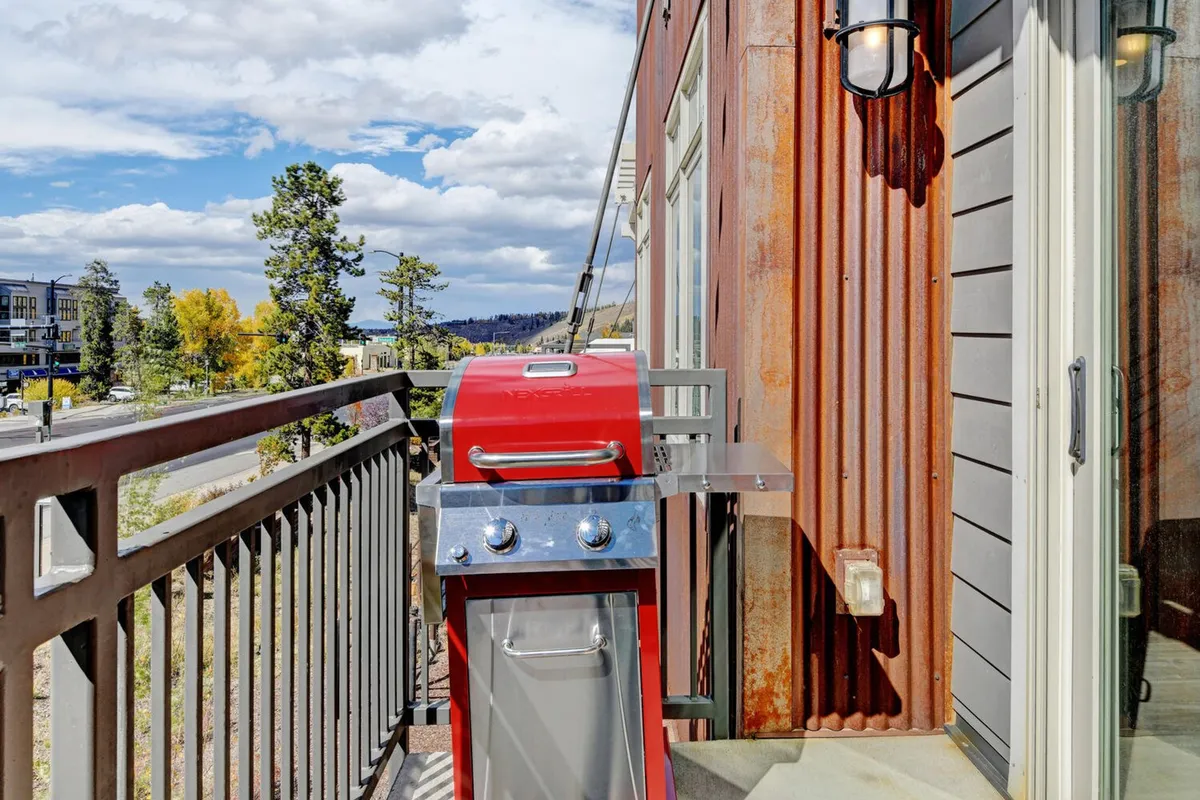 A private deck featuring a red gas grill, balcony railing, and views of trees and mountains in the distance, inviting guests to blend indoor comfort with alfresco fun.